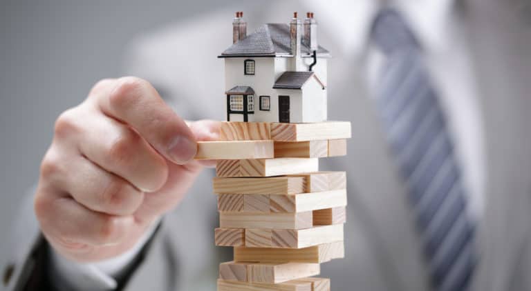 Man in suit touching stack of brown wooden blocks with toy house on top