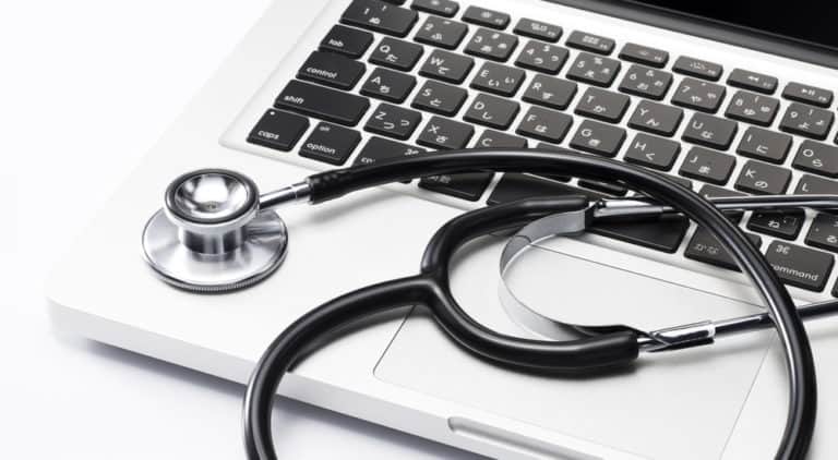 Black and silver stethoscope sitting on keyboard of a silver laptop