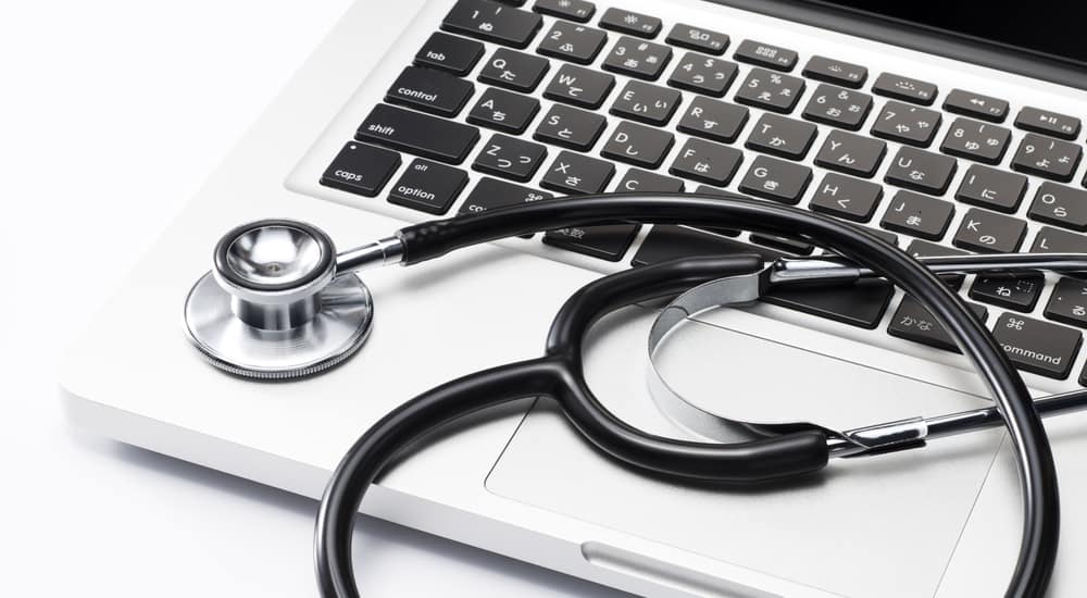 Black and silver stethoscope sitting on keyboard of a silver laptop